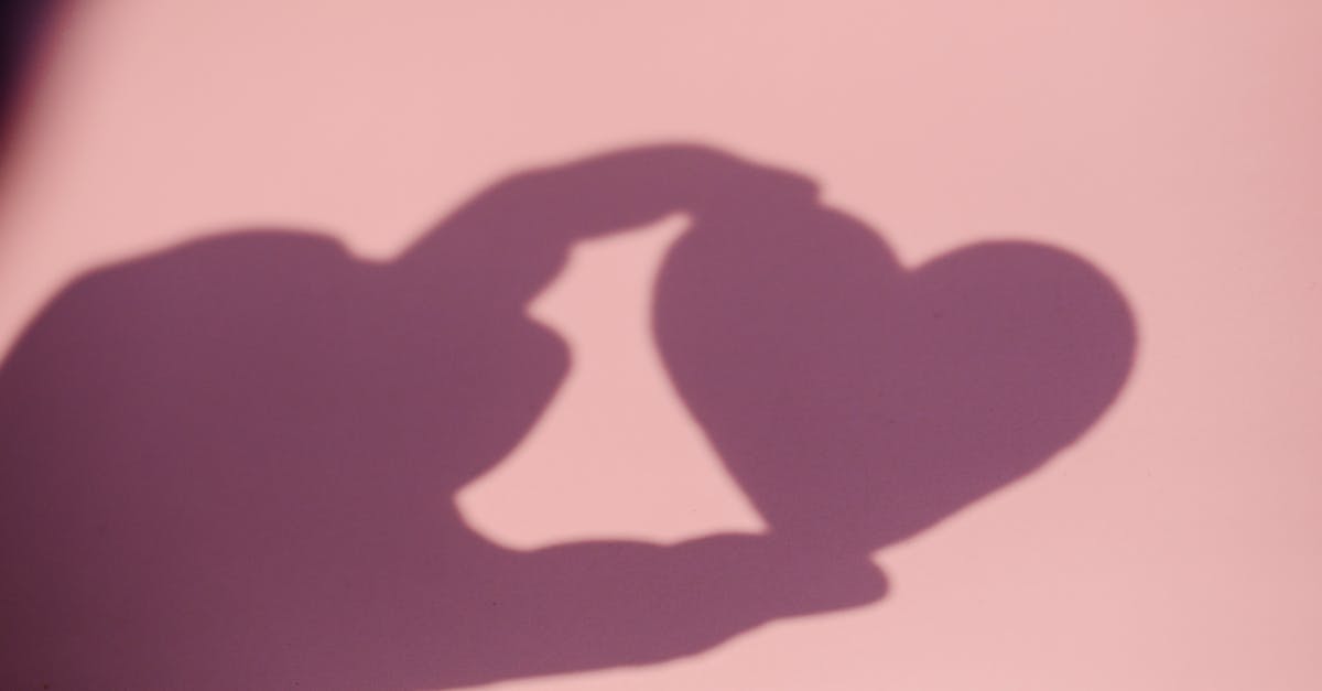 Shadow of a heart shape created by fingers on a pink surface, symbolizing love.